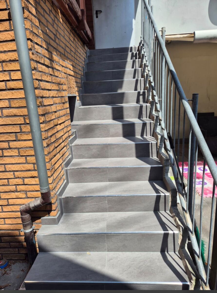 Fertig geflieste Außentreppe mit Geländer an einer Klinkerfassade