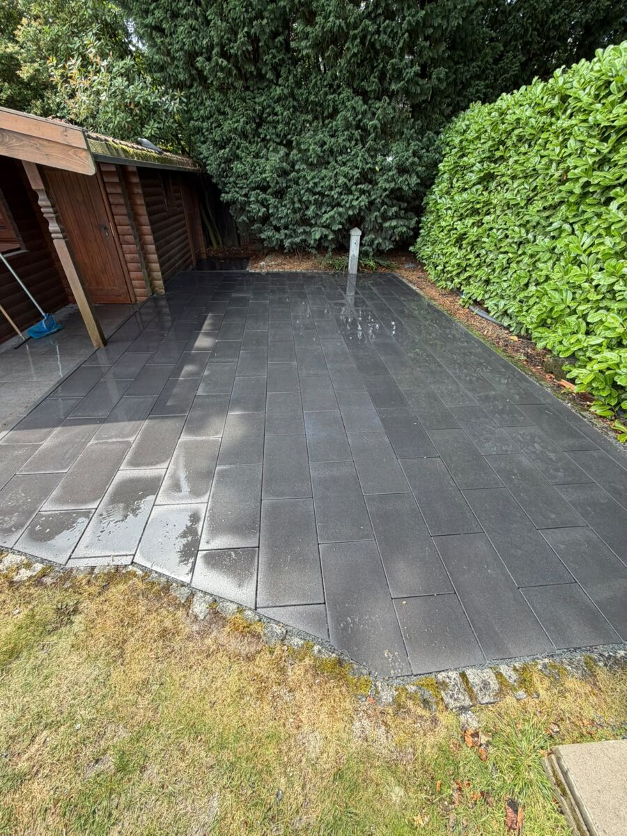 Fertig verlegte dunkle Terrassenplatten entlang einer hohen Hecke