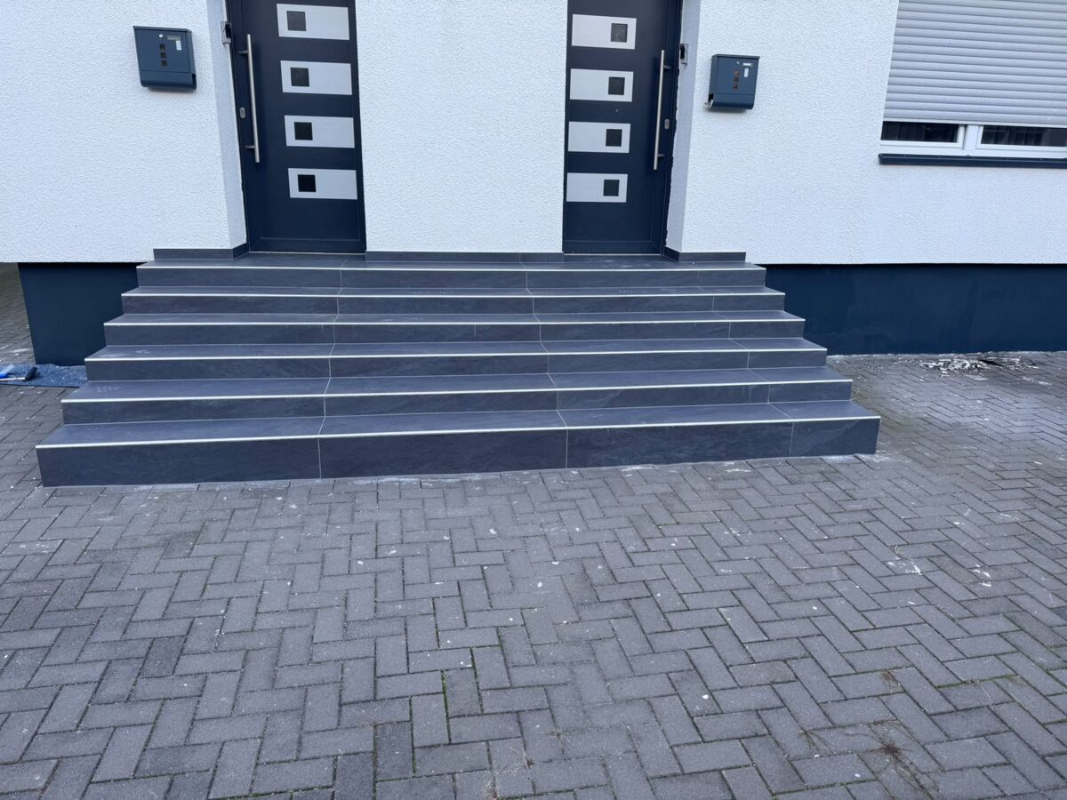 Neu gebaute Eingangstreppe mit dunklen Stufen und gepflastertem Vorplatz